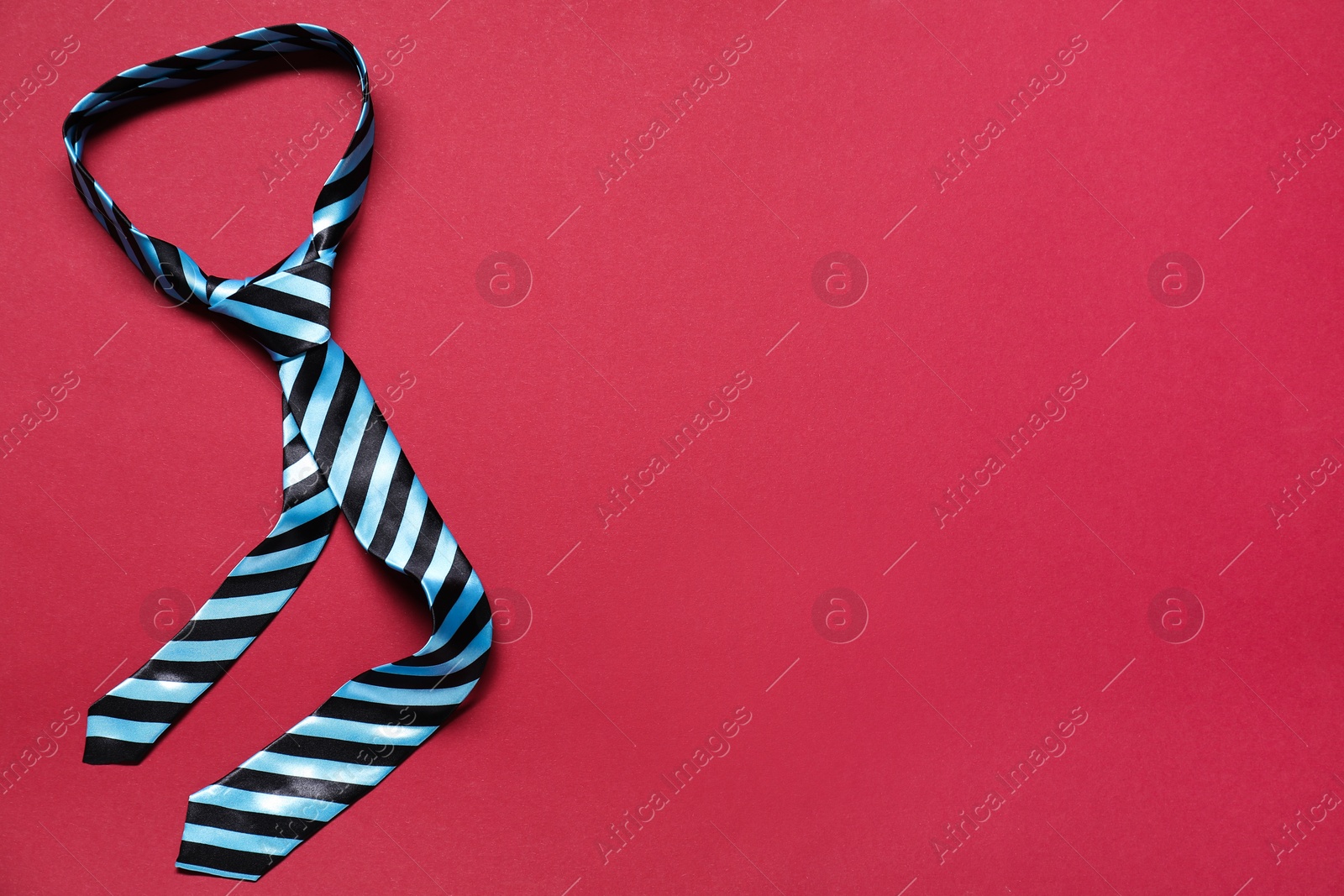 Photo of Stylish striped necktie on red background, top view. Space for text