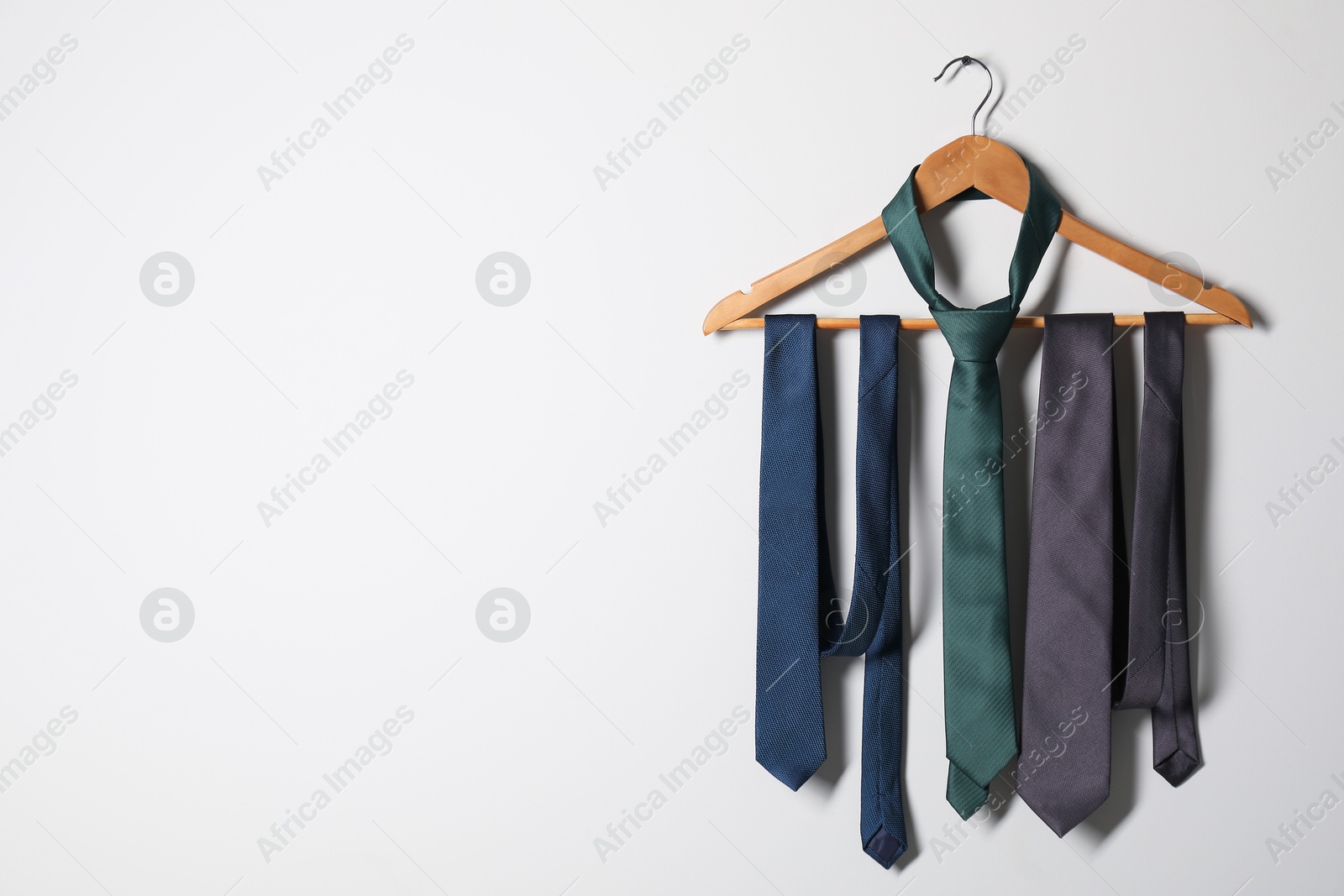 Photo of Hanger with different stylish neckties on light wall. Space for text