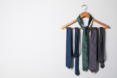Hanger with different stylish neckties on light wall. Space for text