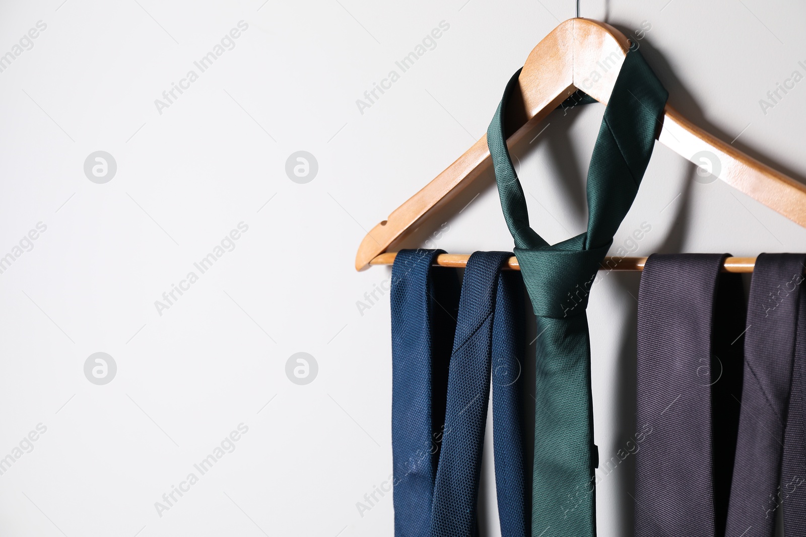 Photo of Hanger with different stylish neckties on light wall. Space for text