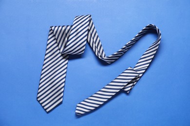 Stylish striped necktie on blue background, top view