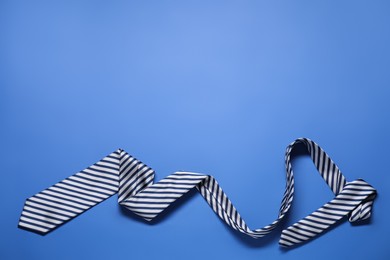 Photo of Stylish striped necktie on blue background, top view. Space for text