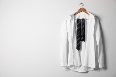 Photo of Hanger with white shirt and striped necktie on light wall, space for text