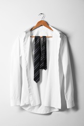 Photo of Hanger with white shirt and striped necktie on light wall