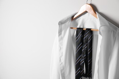 Photo of Hanger with white shirt and striped necktie on light wall, space for text