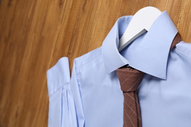Photo of Hanger with light blue shirt and stylish necktie on wooden background, closeup