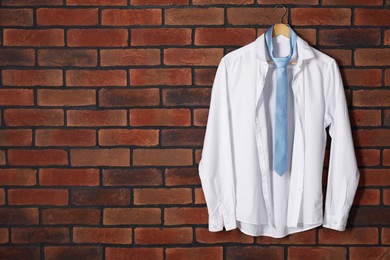 Photo of Hanger with white shirt and light blue necktie on red brick wall. Space for text