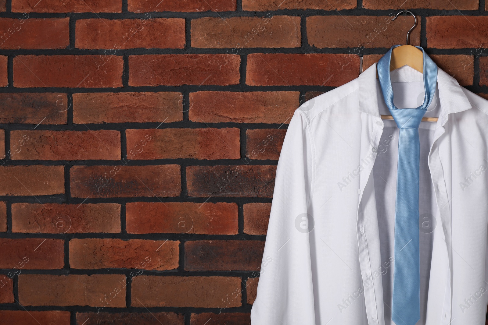 Photo of Hanger with white shirt and light blue necktie on red brick wall. Space for text