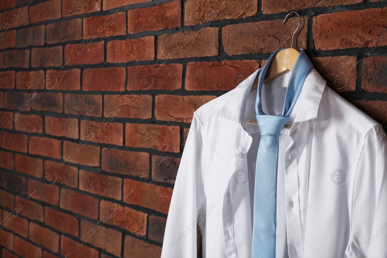 Photo of Hanger with white shirt and light blue necktie on red brick wall. Space for text