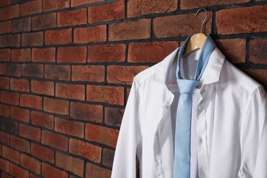 Hanger with white shirt and light blue necktie on red brick wall. Space for text