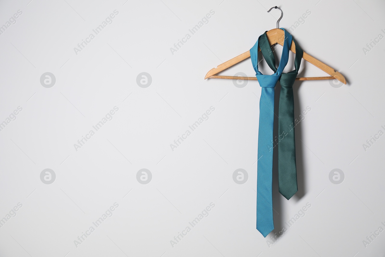 Photo of Hanger with different stylish neckties on light wall. Space for text