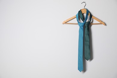 Hanger with different stylish neckties on light wall. Space for text