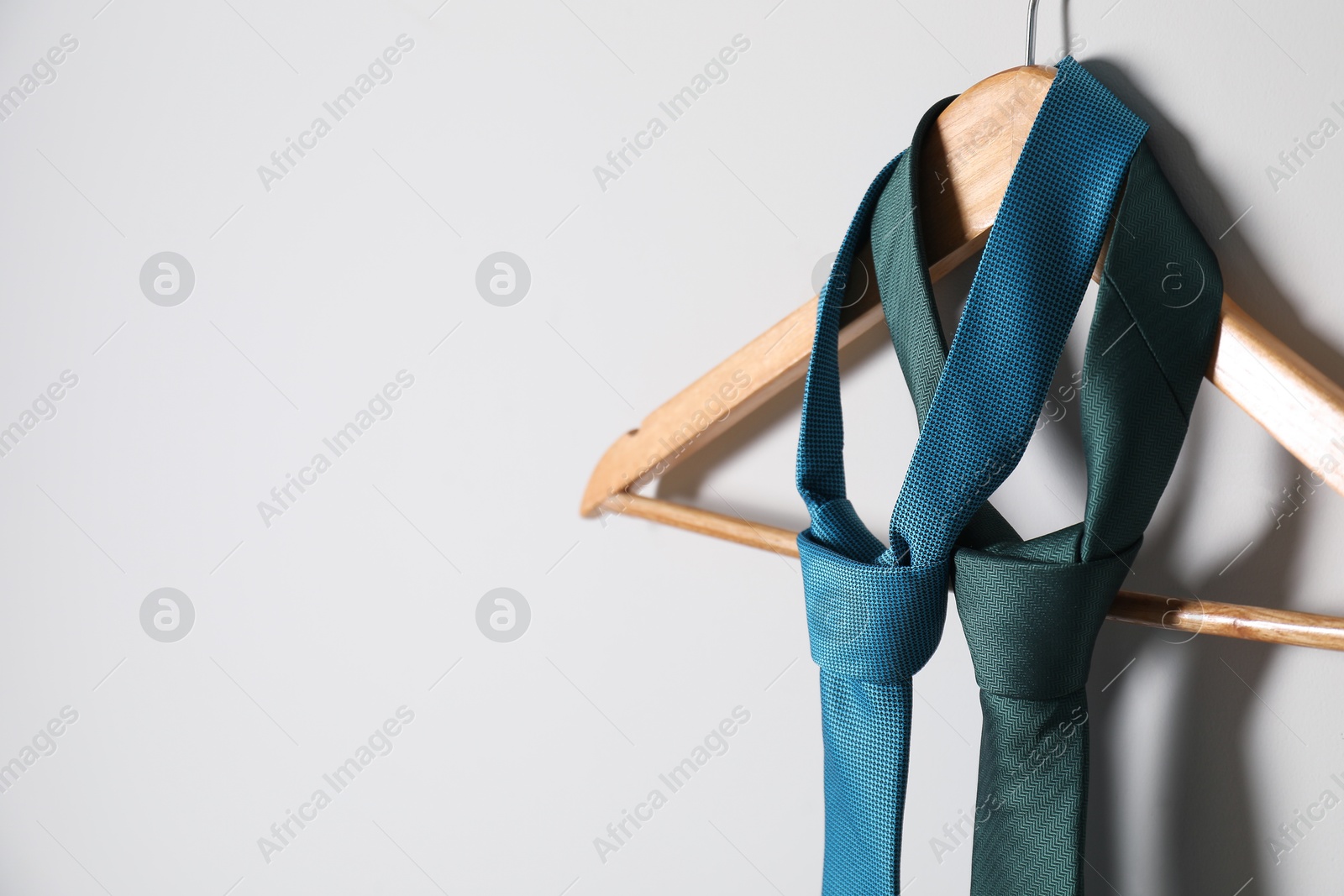 Photo of Hanger with different stylish neckties on light wall. Space for text