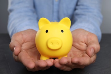 Photo of Man with yellow piggy bank at black table, closeup