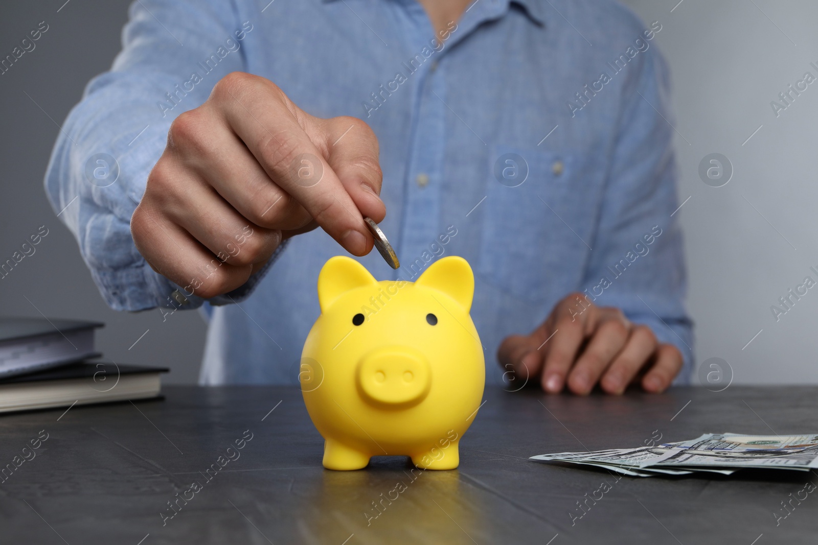 Photo of Man putting coin into yellow piggy bank at black table, closeup