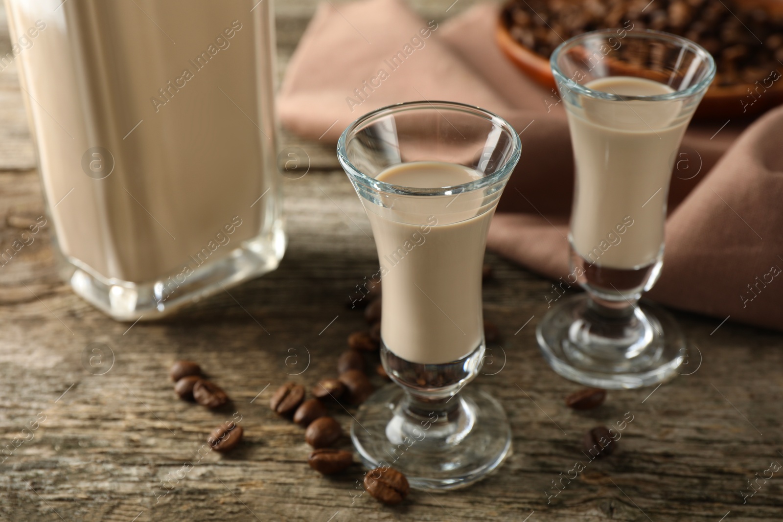 Photo of Coffee cream liqueur in glasses and beans on wooden table, closeup