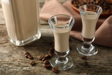 Photo of Coffee cream liqueur in glasses and beans on wooden table, closeup