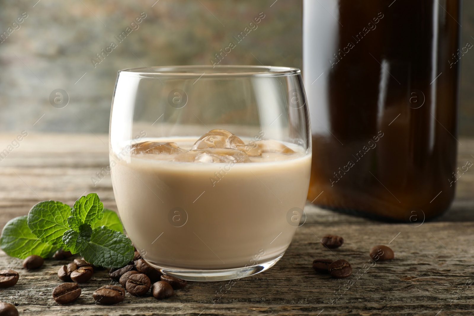 Photo of Coffee cream liqueur in glass, mint and beans on wooden table, closeup