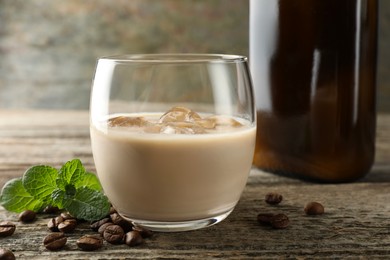 Coffee cream liqueur in glass, mint and beans on wooden table, closeup