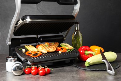 Photo of Electric grill with different products and knife on grey textured table