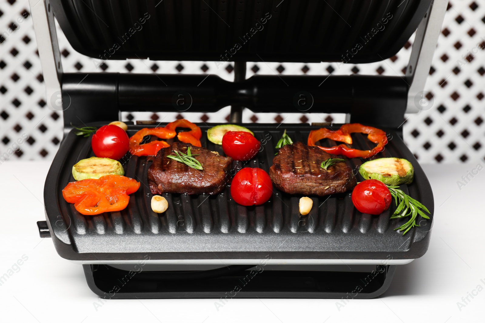 Photo of Electric grill with tasty meat, spices and vegetables on white table