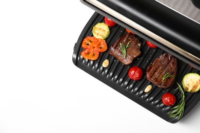 Electric grill with tasty meat, spices and vegetables on white table, top view. Space for text