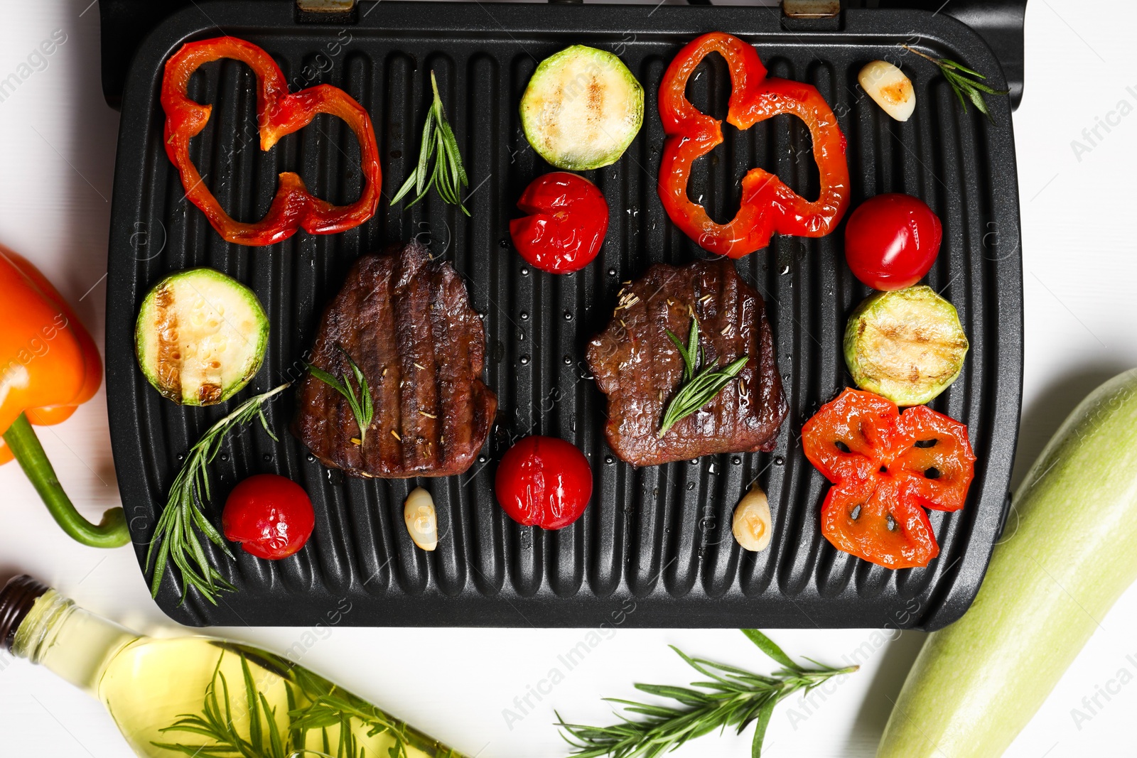 Photo of Electric grill with tasty meat, spices and vegetables on white table, flat lay