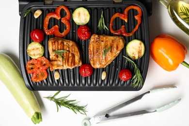 Electric grill with tasty meat, spices and vegetables on white table, flat lay