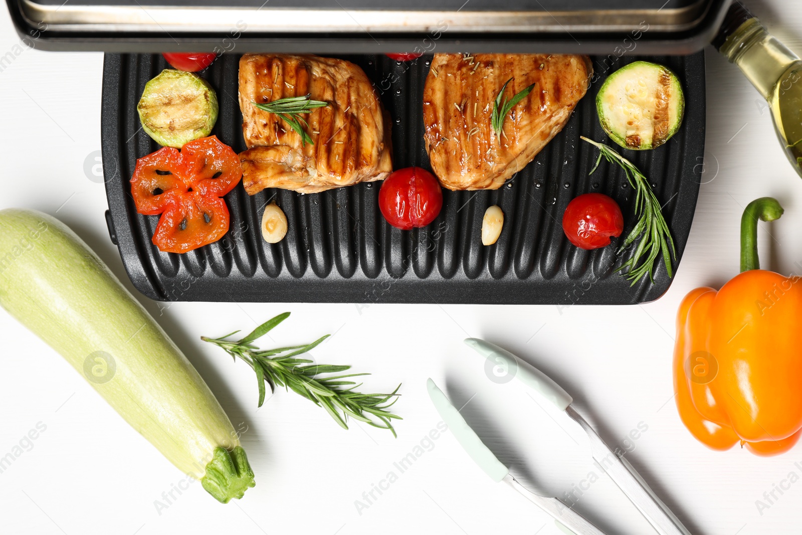 Photo of Electric grill with tasty meat, spices and vegetables on white table, flat lay