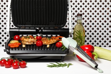 Photo of Electric grill with different products and tongs on white table