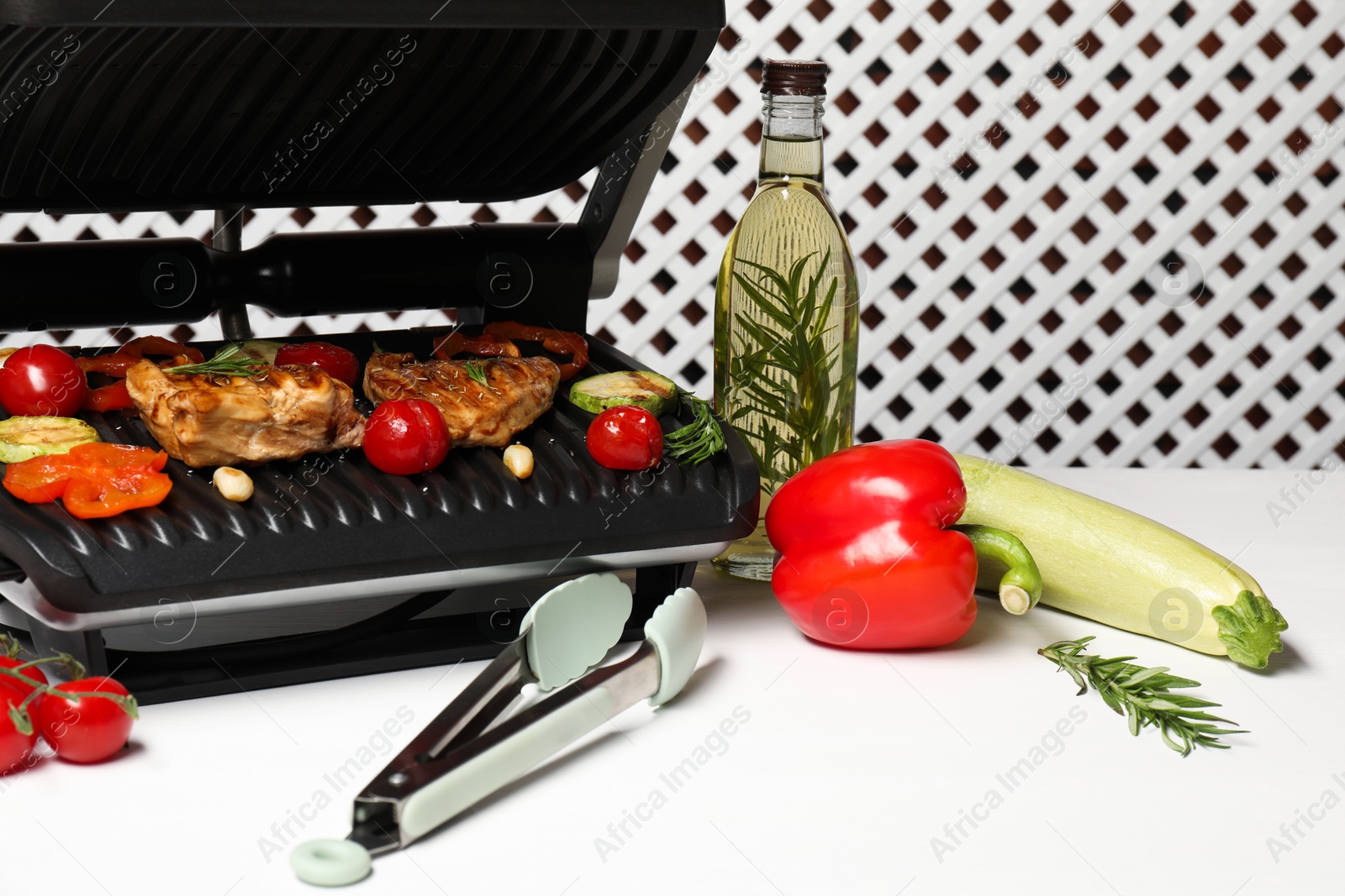 Photo of Electric grill with different products and tongs on white table