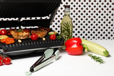 Electric grill with different products and tongs on white table