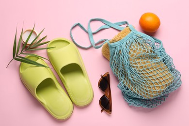 String bag with towel, sunglasses, orange, slippers, cream and palm leaf on pink background, flat lay