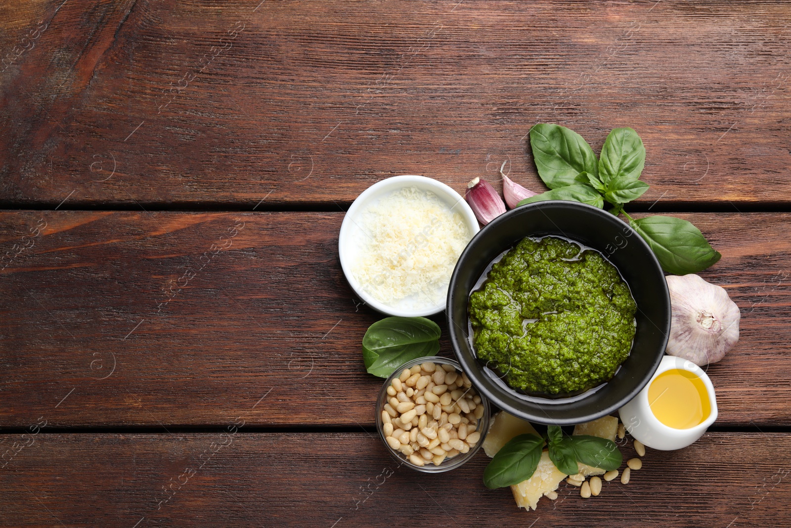 Photo of Tasty pesto sauce in bowl, basil, pine nuts, cheese, garlic and oil on wooden table, top view. Space for text