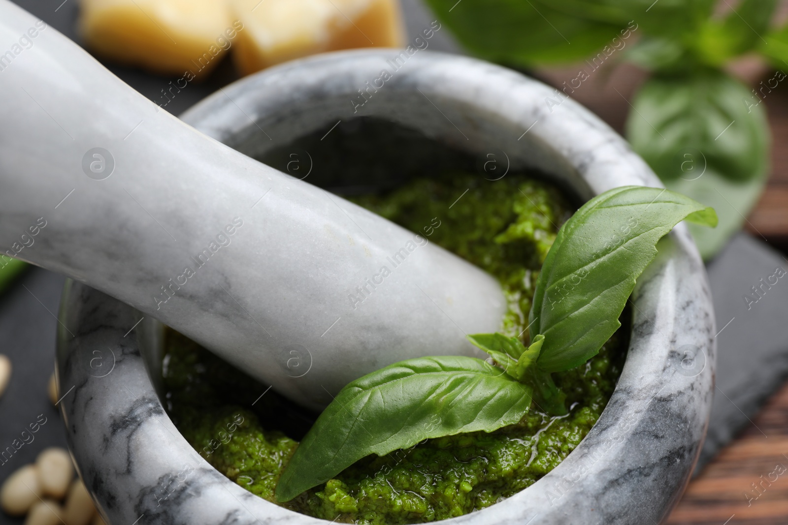 Photo of Tasty pesto sauce in mortar, pestle and basil on table, closeup