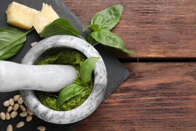 Photo of Tasty pesto sauce in mortar, pestle, basil, pine nuts and cheese on wooden table, top view. Space for text