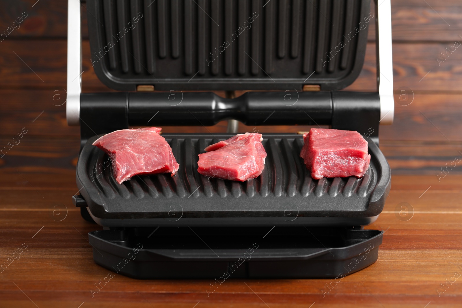 Photo of Electric grill with raw meat on wooden table