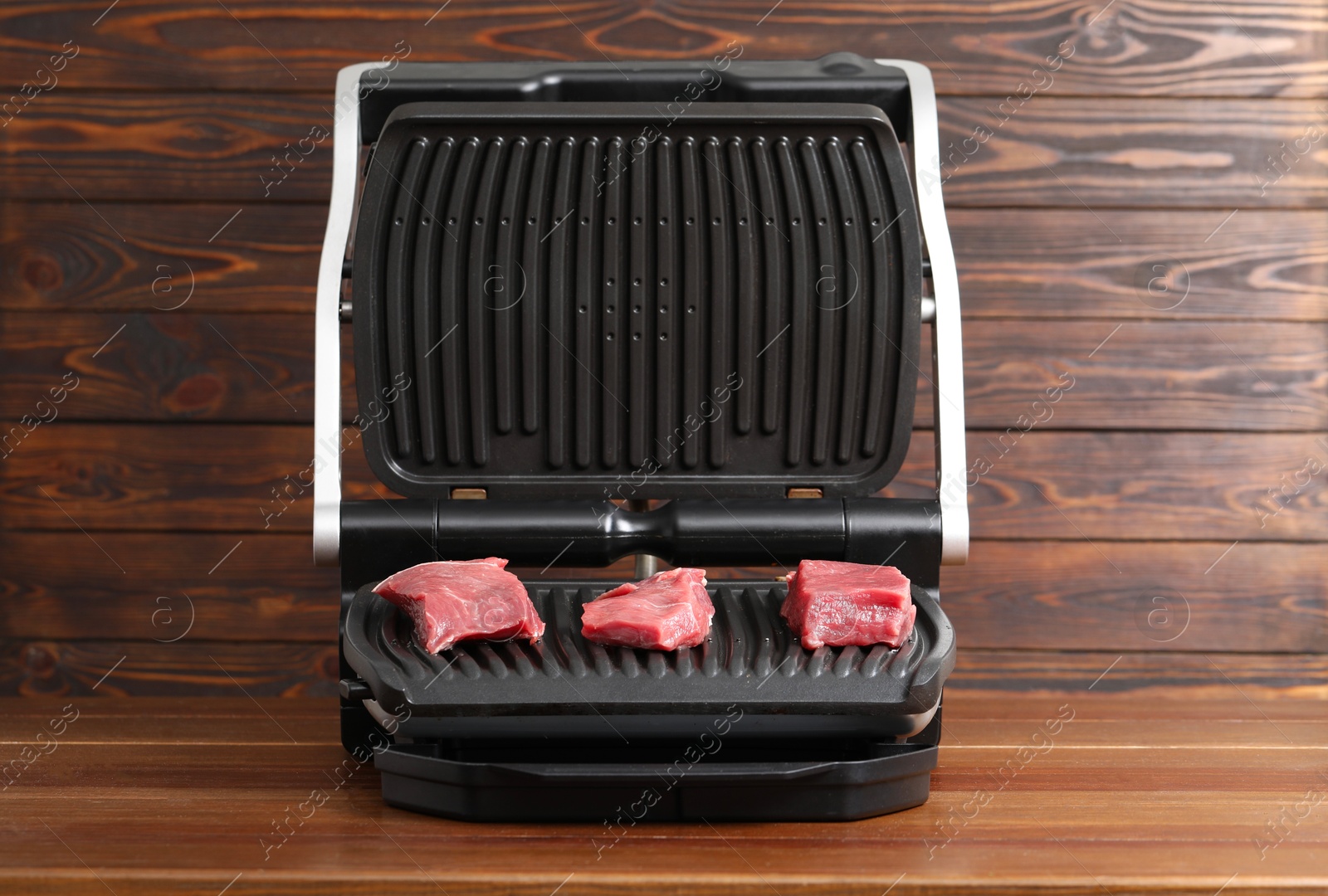 Photo of Electric grill with raw meat on wooden table