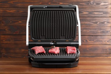 Photo of Electric grill with raw meat on wooden table