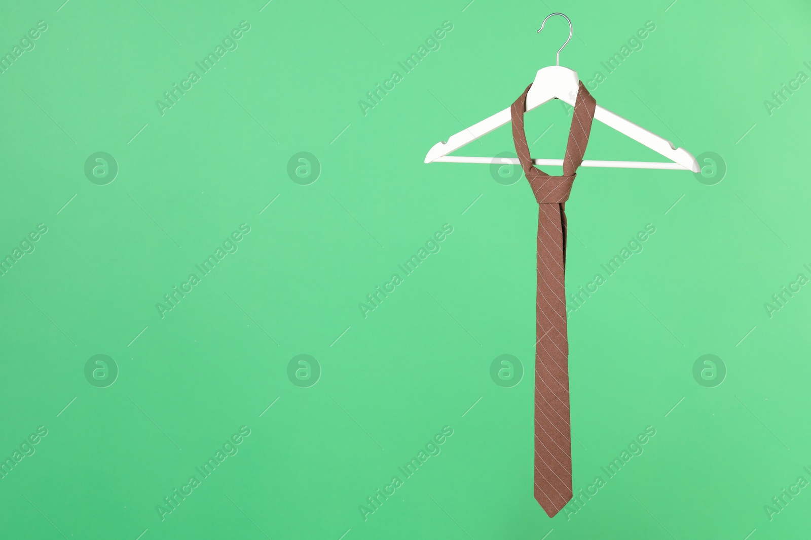 Photo of Hanger with brown striped tie on green background. Space for text