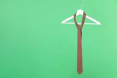 Hanger with brown striped tie on green background. Space for text