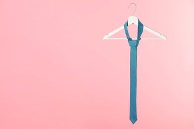 Hanger with turquoise tie on pink background. Space for text