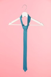 Hanger with turquoise tie on pink background