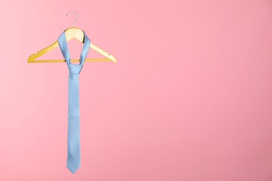Photo of Hanger with light blue tie on pink background. Space for text