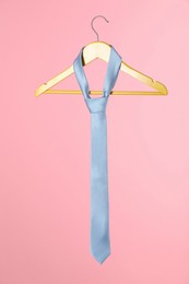 Photo of Hanger with light blue tie on pink background