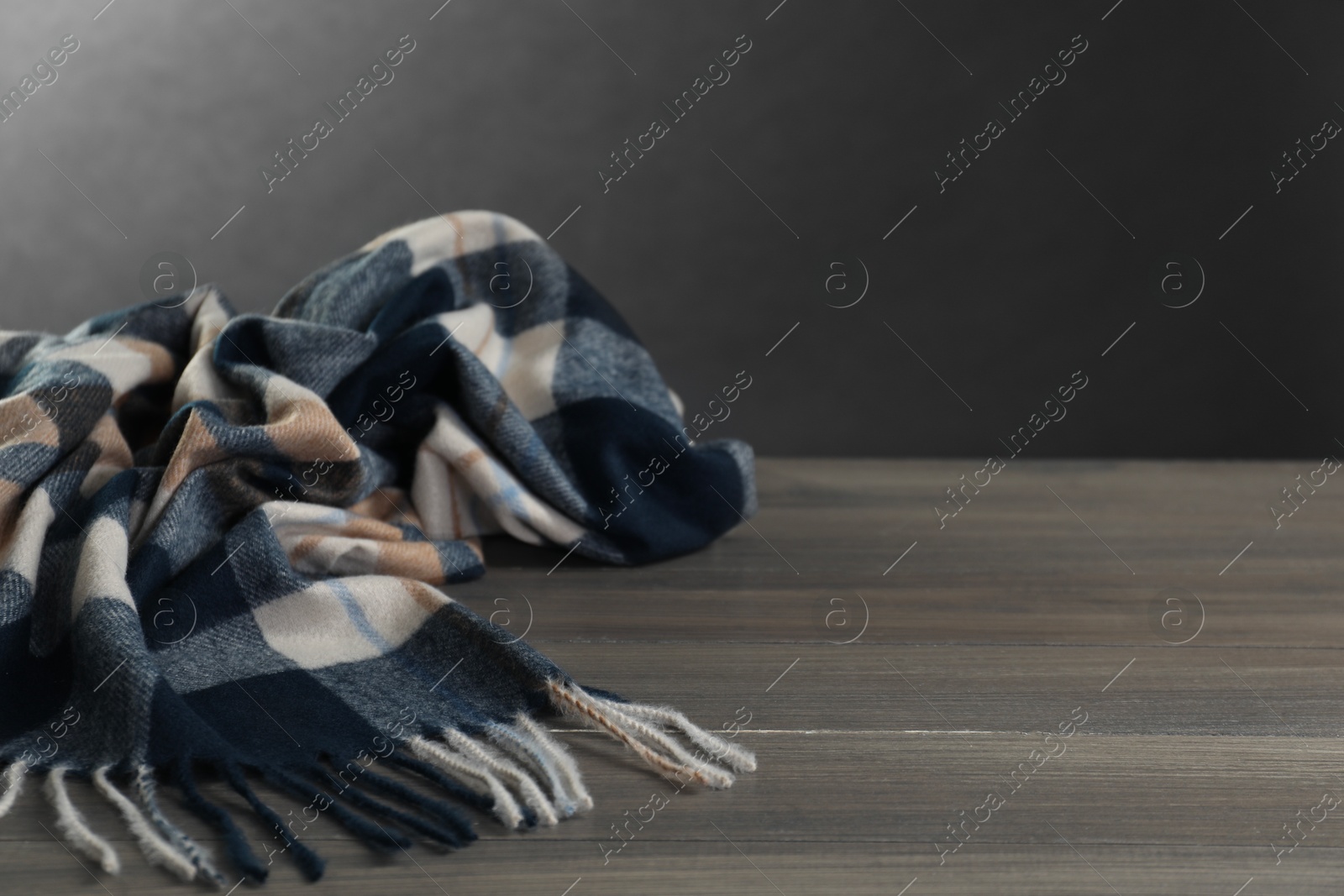 Photo of Soft checkered scarf on wooden table against gray background, space for text
