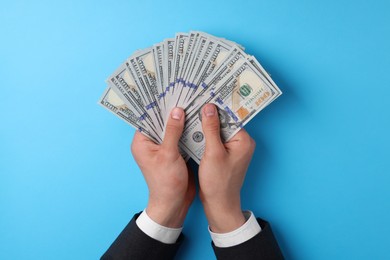 Photo of Money exchange. Man holding dollar banknotes on light blue background, top view