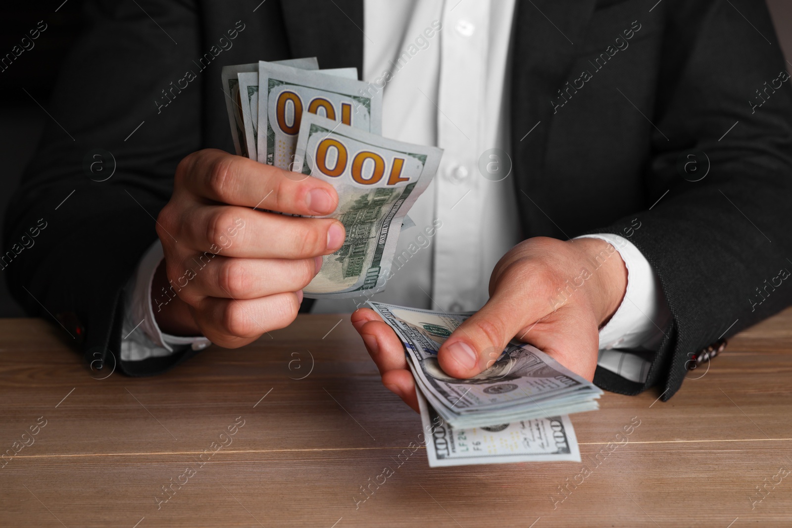 Photo of Money exchange. Man counting dollar banknotes at wooden table, closeup