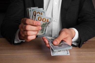 Money exchange. Man counting dollar banknotes at wooden table, closeup