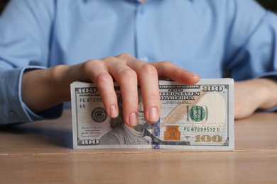 Photo of Money exchange. Woman holding dollar banknotes at wooden table, closeup